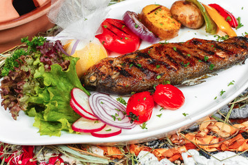 Mediterranean dish, Georgian recipe. Baked river fish with lemon, vegetables, pepper and grilled tomatoes with spices.