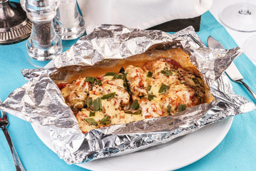 Seafood, Mediterranean cuisine, European dish. Fish baked in a foil with tomatoes, entirely with onion rings, red and green peppers, chili peppers, greens, cheese, mushrooms and vegetables. Caucasian 