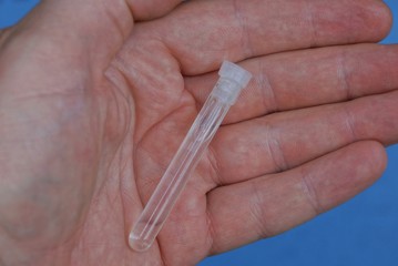 a small long white glass bottle test tube with liquid lies on the palm of the hand