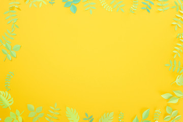 top view of paper cut green tropical leaves on yellow bright background with copy space