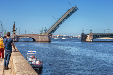 a group of tourists watching the rise of the Trinity bridge in St. Petersburg before the passage of the warships participating in the parade