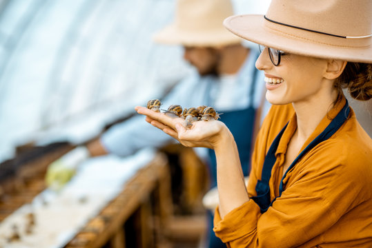 Close-up portrait of a young woman holding snails, taking care of them in the farm for snails growing