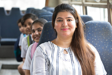 Fototapeta premium Happy teacher taking care of schoolgirl while traveling in school bus