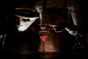 Bartender pouring cocktail with sieve in glass
