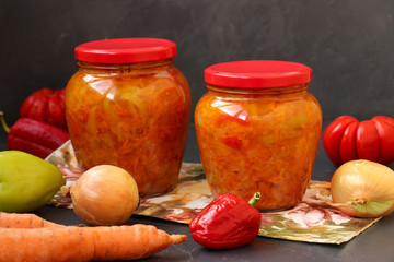 Vegetable salad of carrots, peppers, onions and tomatoes for winter is located on a table on a dark background