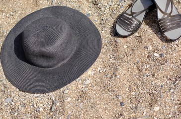 A black straw hat and flip flops lying on the sand on the beach. Beach, vacation, summer concept....