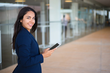 Fototapeta na wymiar Happy confident professional using tablet in office hall. Young Latin business woman holding tablet and smiling at camera. Communication concept