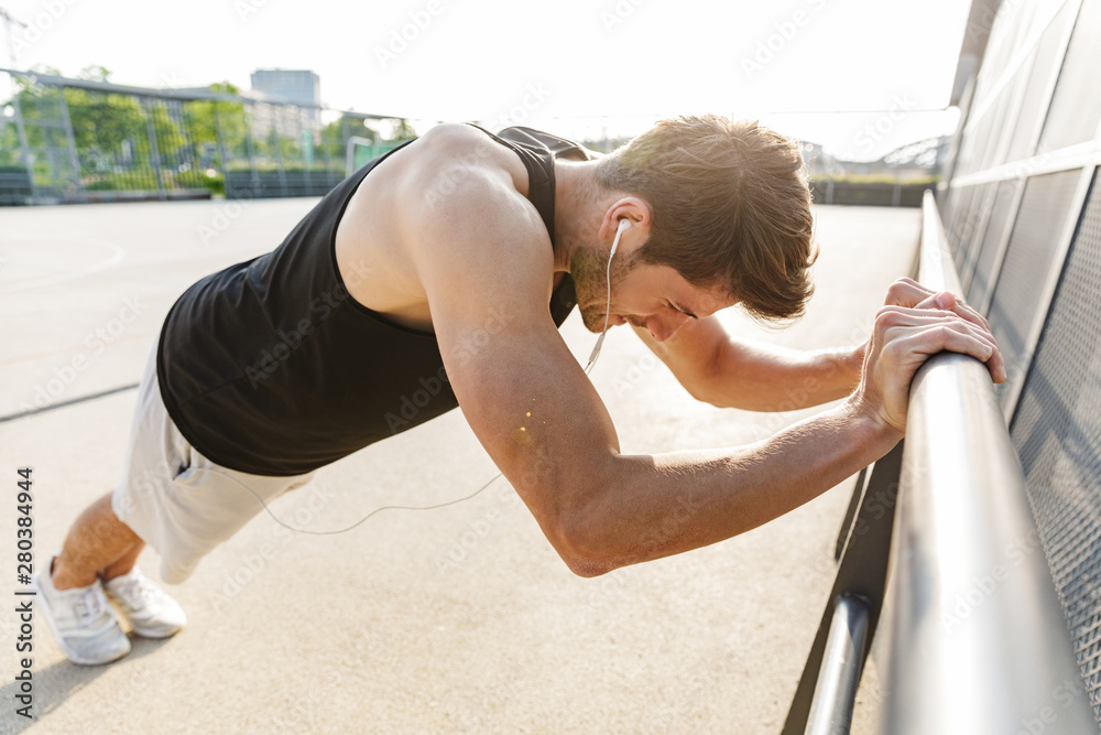 Wall mural Photo of caucasian man wearing earphones standing on sports ground during morning workout outdoors