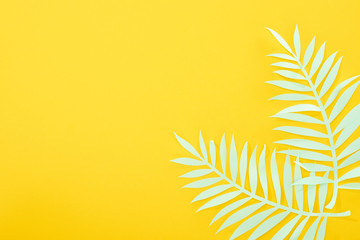 top view of paper cut green tropical leaves on yellow bright background with copy space