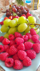 Delicious fresh organic fruits on a plate: raspberries and green grapes
