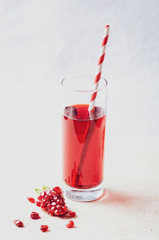 Pomegranate  juice  in glass with seeds, fruits and leaves on light marble table.