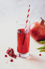 Pomegranate  juice  in glass with seeds, fruits and leaves on light marble table.