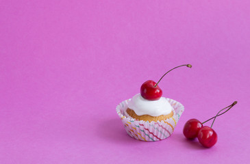 Cupcake with red cherry on pink background with copy space.