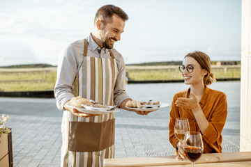 Waiter serving delicious dish with stuffed snails to a young woman client at the restaurant outdoors. Restaurant with own production of snails