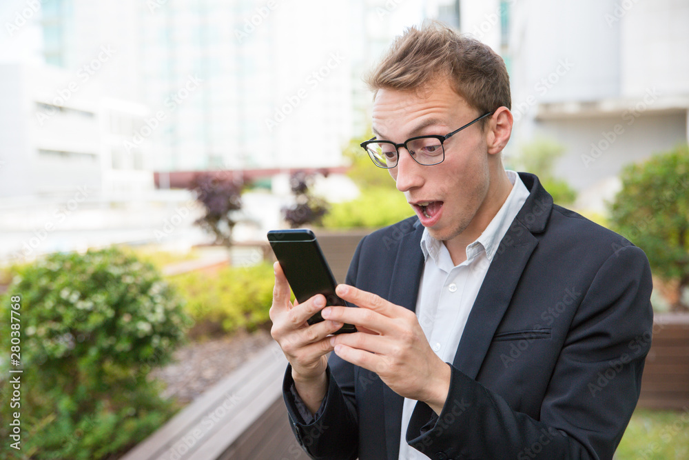 Wall mural excited office employee with cellphone getting shocking news. amazed business man in eyeglasses and 