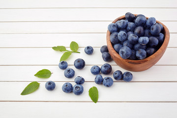 Fresh raw blueberries with leaves on white wooden background. Organic food