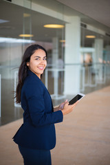 Fototapeta na wymiar Positive joyful manager using tablet in office hall. Young Latin business woman holding tablet and smiling at camera. Wireless connection concept
