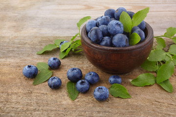 Fresh raw blueberries with leaves on white wooden background. Organic food