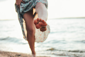 Crop photo of legs of romantic young woman in dress on beach, summer vacation time