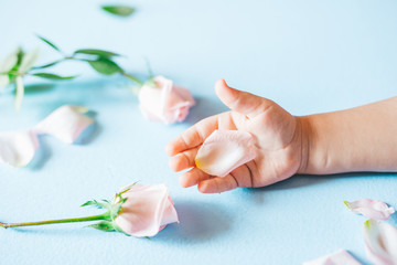 Obraz na płótnie Canvas Fashion art hand of a little child holding flowers on it blue background