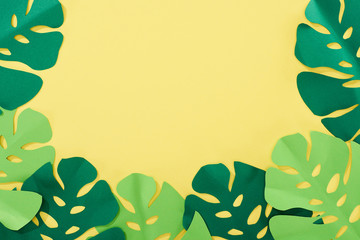 top view of paper cut green tropical leaves on yellow bright background with copy space