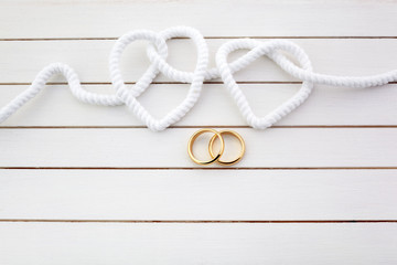 Double heart shaped whiter rope and a double gold ring on white wooden background