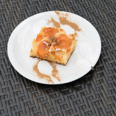 Tasty apricot cake on a white dishware, where a mask of two forks and two spoons with cinnamon and powdered sugar is visible. At the edge of the plate a fly is tasting the powdered sugar.