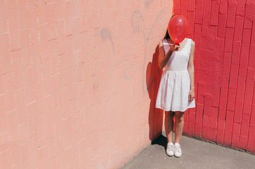 Woman Hiding Her Face Behind A Red Balloon on pink wall