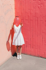 Woman Hiding Her Face Behind A Red Balloon on pink wall