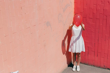 Woman Hiding Her Face Behind A Red Balloon on pink wall
