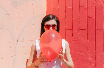 Woman Hiding Her Face Behind A Red Balloon on pink wall
