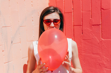 Woman Hiding Her Face Behind A Red Balloon on pink wall