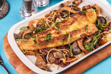 Seafood, Mediterranean cuisine. Grilled fish steak with mushrooms, oyster mushrooms, boletus, greens and onion rings. Caucasian kitchen