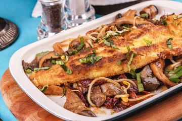 Seafood, Mediterranean cuisine. Grilled fish steak with mushrooms, oyster mushrooms, boletus, greens and onion rings. Caucasian kitchen