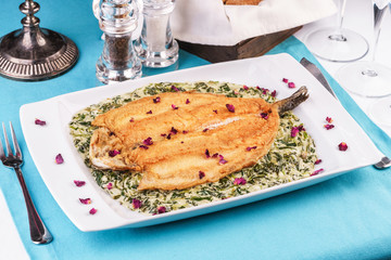 Fried steak of sea fish in batter, in a creamy sauce with greens and rose petals. Caucasian cuisine, Mediterranean food