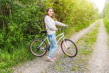 Fototapeta premium Young woman riding bicycle in summer city park outdoors. Active people. Hipster girl relax and rider bike. Cycling to work at summer day. Bicycle and ecology lifestyle concept