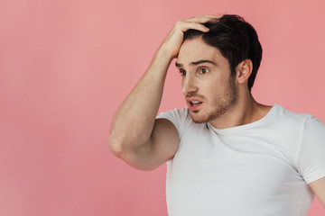 shocked muscular man in white t-shirt touching head isolated on pink