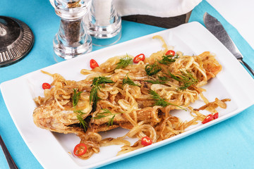 Fried sea fish pike perch is served under onion rings, chili peppers and greens according to the Georgian recipe. Mediterranean Kitchen