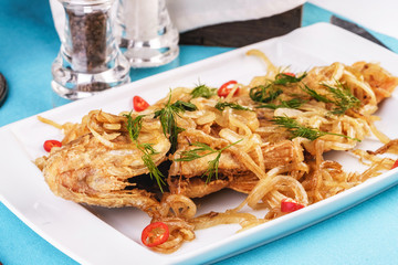 Fried sea fish pike perch is served under onion rings, chili peppers and greens according to the Georgian recipe. Mediterranean Kitchen