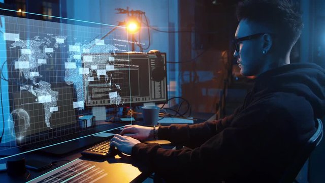 cybercrime, hacking and technology concept - asian male hacker in dark room writing code or using computer virus program for cyber attack