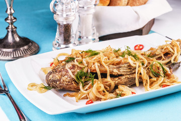 Fried sea fish pike perch is served under onion rings, chili peppers and greens according to the Georgian recipe. Mediterranean Kitchen