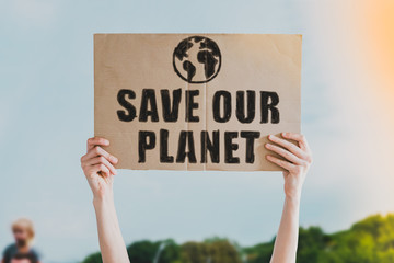 Person holding brown save our planet cardboard poster. Save the planet on a paper banner in men's...