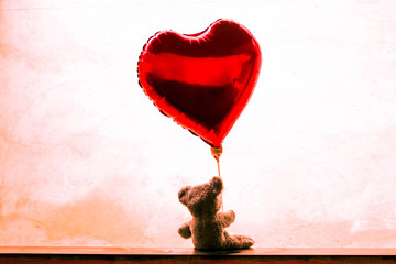 Urso de pelúcia sentado segurando um balão de coração vermelho