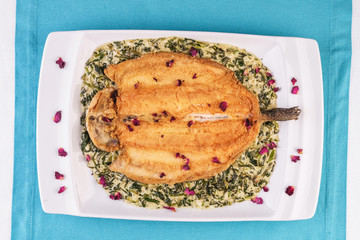 Fried steak of sea fish in batter, in a creamy sauce with greens and rose petals. Caucasian cuisine, Mediterranean food