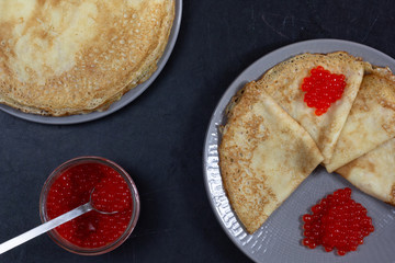 Blini triangles or crepes with red caviar on the plate with jar