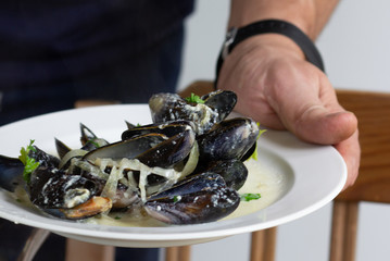 Cooked mussels in wine and cream with greens and onion served on white plate
