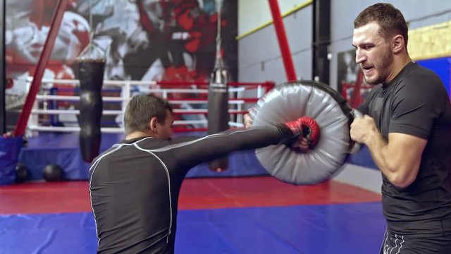 Man mma trainer exercising with athlete in a gym. Athlete training his punches on a boxing bag