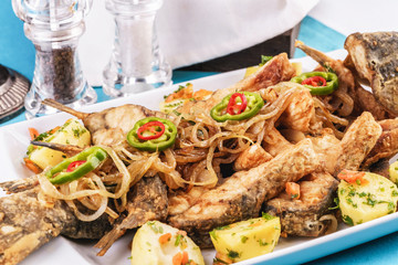Seafood, Mediterranean cuisine. Baked fish with potatoes, onion rings, chili pepper, lemon and greens. Caucasian kitchen