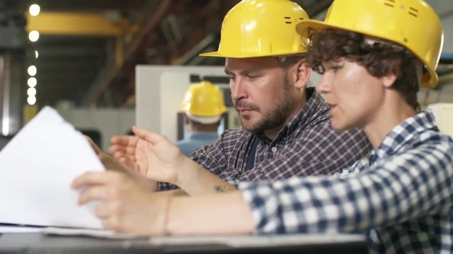 Pan chest-up shot of female and male factory engineers standing in modern automated production facility and studying data sheets with technical specifications, engaged in animated discussion