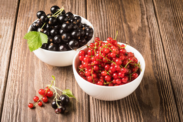 Fresh ripe red black currant berry in white bowls on wooden background. Horizontal frame.